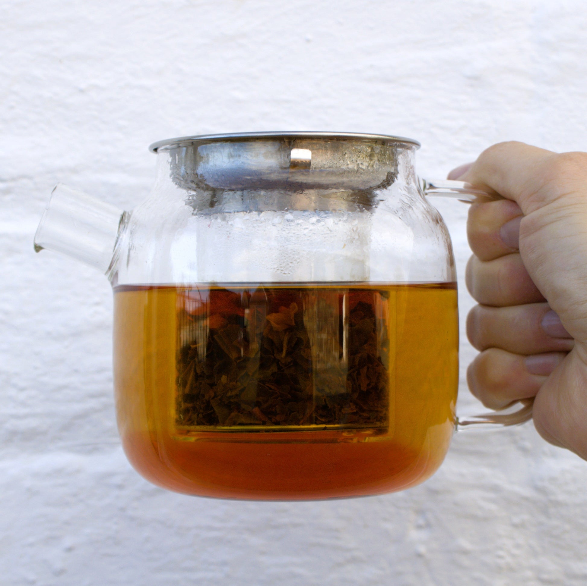 Hand holding a glass teapot filled with tea against a white background